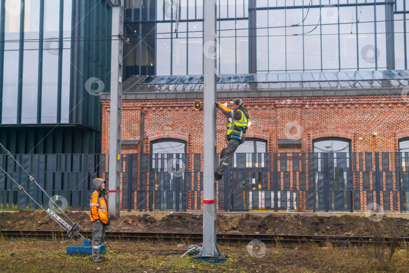 Скачать Рабочие устанавливают систему оповещения на столбе на железной дороге на фоне промышленных зданий. фотосток Ozero