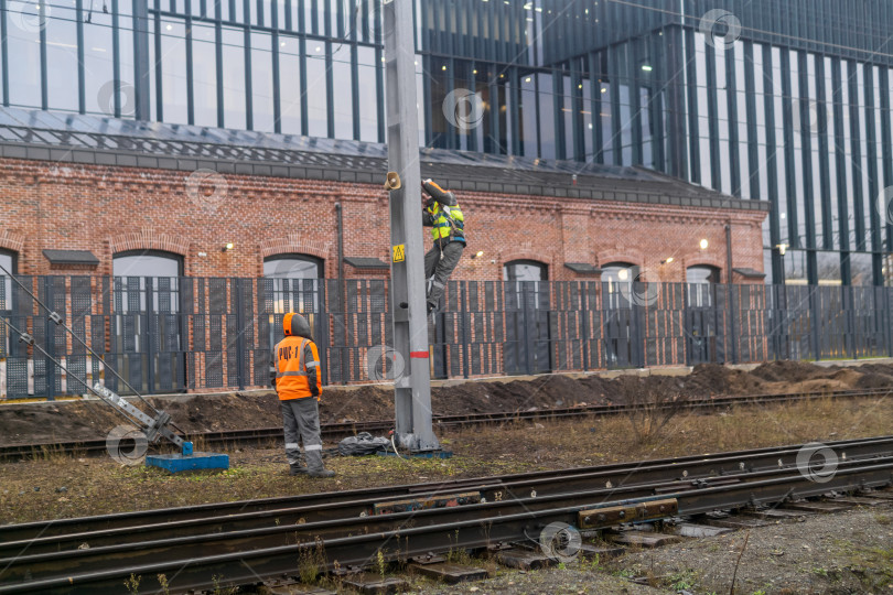 Скачать Рабочие устанавливают систему оповещения на столбе на железной дороге на фоне промышленных зданий. фотосток Ozero