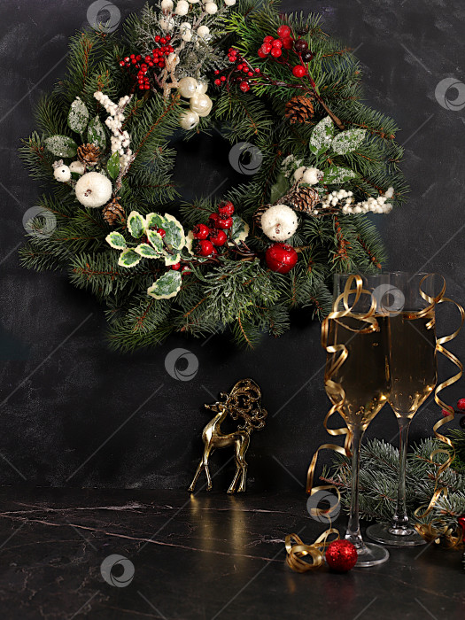 Скачать Шампанское, праздничные украшения и еловый венок со статуэткой оленя на элегантном фоне - концепция кануна Рождества. Новогодняя открытка, баннер для демонстрации, Поздравление с Новым годом фотосток Ozero