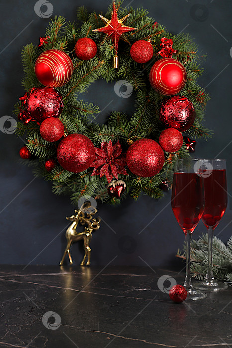 Скачать Шампанское, праздничные украшения и еловый венок со статуэткой оленя на элегантном фоне - концепция кануна Рождества. Новогодняя открытка, баннер для демонстрации, Поздравление с Новым годом фотосток Ozero