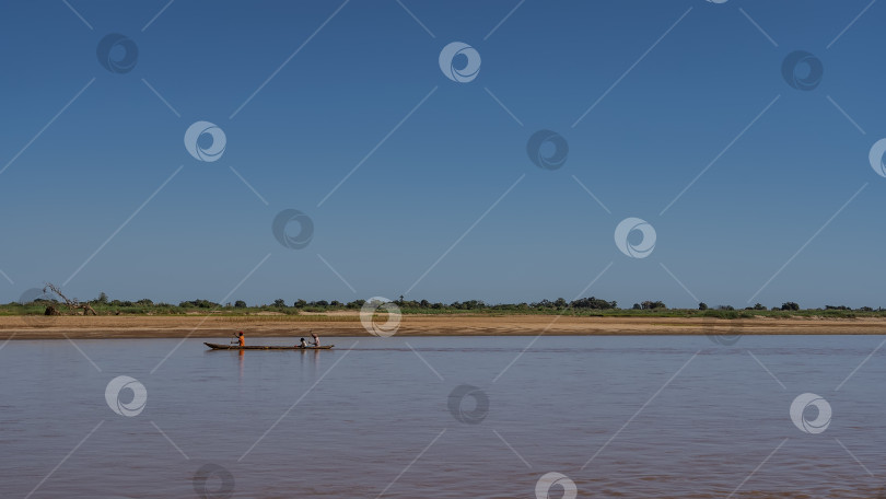Скачать Традиционная деревянная лодка-пирога с людьми плывет по красно-коричневой реке. фотосток Ozero