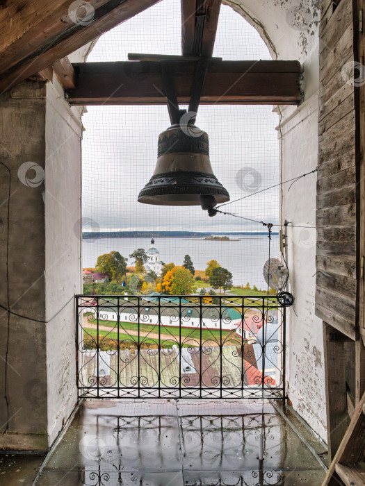 Скачать Панорамный вид с колокольни Нило-Столбенского монастыря на озеро Селигер и территорию монастыря. Колокол и кованое ограждение на фоне созерцательного осеннего пейзажа. фотосток Ozero