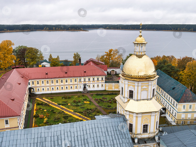 Скачать Панорамный вид с колокольни Нило-Столбенского монастыря на внутренний двор и озеро Селигер. Золотой купол Петропавловской церкви, монастырские корпуса с красными крышами и осенние цветочные дорожки передают созерцательное настроение. фотосток Ozero