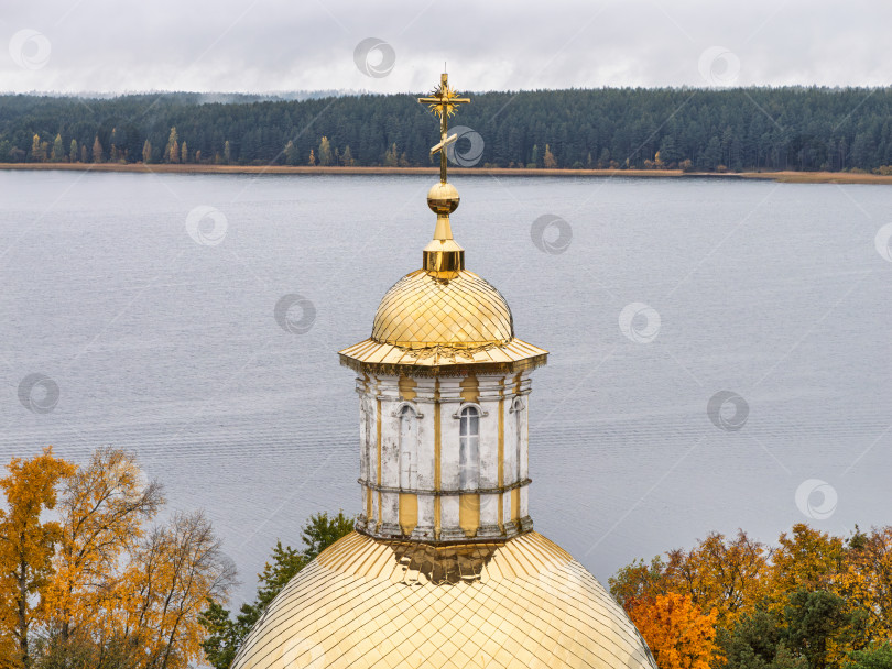 Скачать Крупный план золотого православного креста на куполе Петропавловской церкви в Нило-Столбенском монастыре. Величественный вид на озеро Селигер и осенний лес на горизонте передает созерцательное настроение. фотосток Ozero