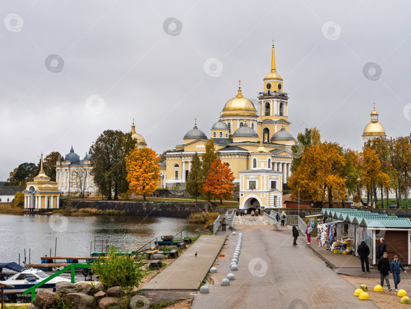Скачать Осенний панорамный вид на Нило-Столбенский монастырь (Нилова пустынь) с насыпного моста на озере Селигер. Осенний пейзаж, золотые купола, туристы и лодки. фотосток Ozero