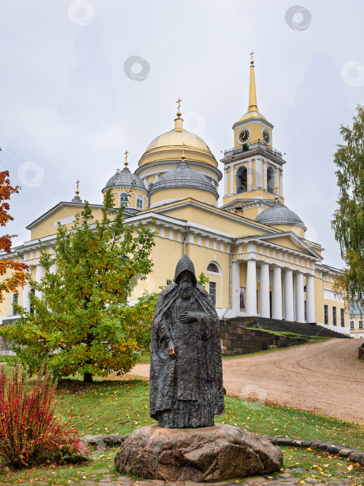 Скачать Вертикальный кадр: Памятник Нилу Столобенскому на фоне главного собора Нило-Столбенского монастыря (Нилова пустынь). Осенний пейзаж и атмосфера умиротворения. фотосток Ozero