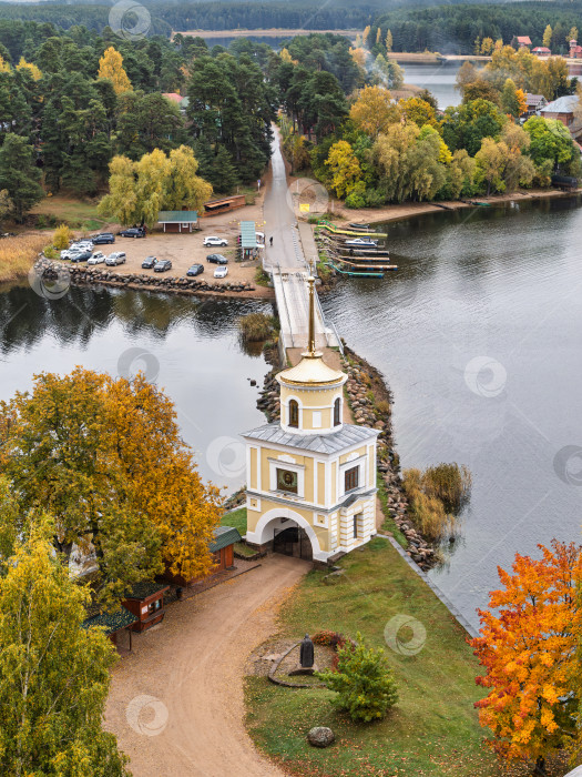 Скачать Величественный панорамный вид с колокольни Нило-Столбенского монастыря на озеро Селигер. Светлицкая башня и мост-насыпь, изрезанный берег с пришвартованными лодками, парковка и живописные осенние деревья передают созерцательное настроение. фотосток Ozero
