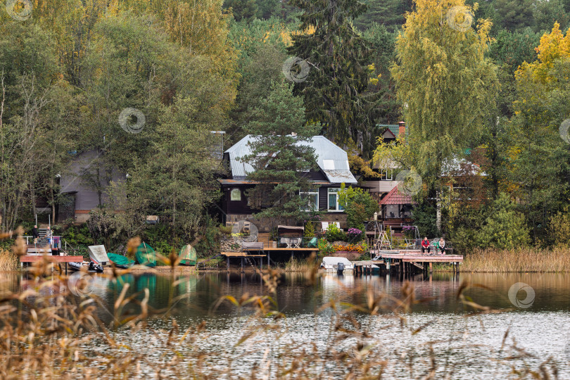 Скачать Панорамный вид на частные дома и коттеджи в лесном массиве на берегу озера Селигер. Осенний пейзаж с деревянными пирсами и лодками. фотосток Ozero