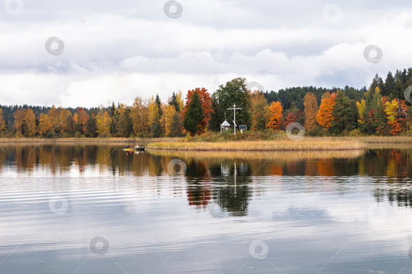 Скачать Остров с крестом и лодка на зеркальной глади озера Селигер. Живописный осенний пейзаж. фотосток Ozero