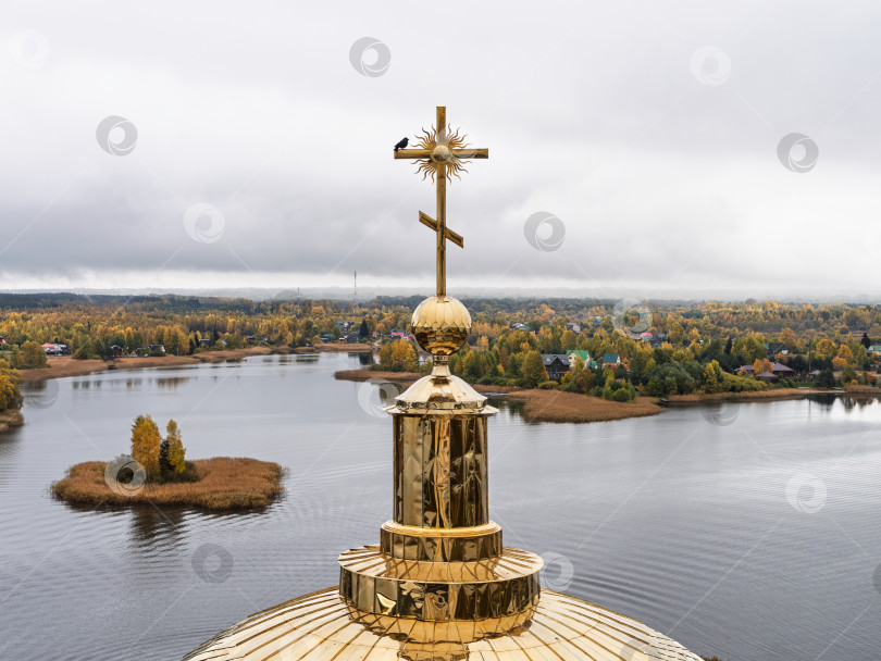 Скачать Величественный панорамный вид с колокольни Нило-Столбенского монастыря на озеро Селигер. Золотой православный крест с вороной на куполе, островок и живописная деревня на изрезанном берегу, окруженная осенними деревьями. фотосток Ozero