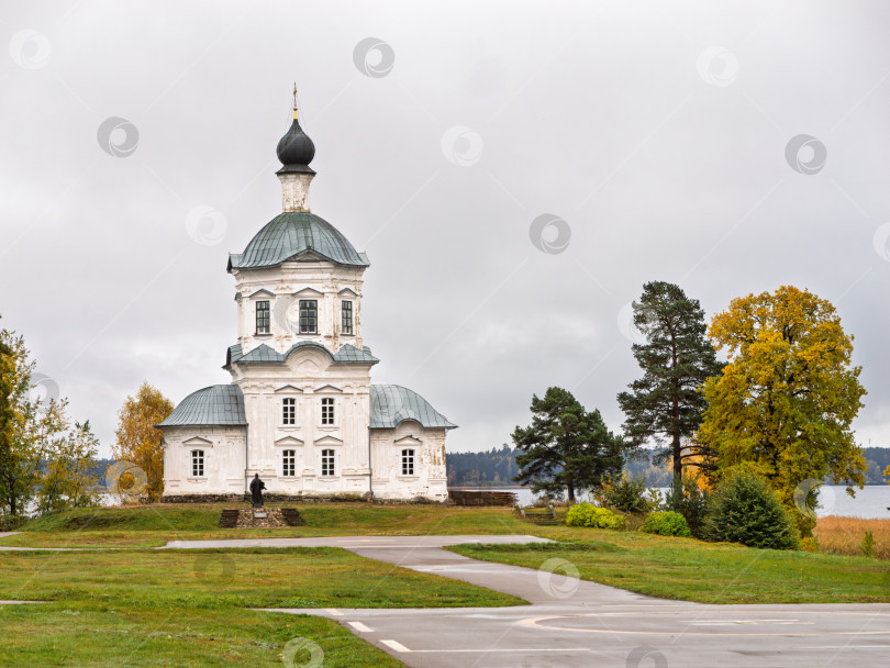 Скачать Живописный осенний пейзаж с Крестовоздвиженской церковью Нило-Столбенского монастыря (Нилова пустынь). Белокаменное здание с темным куполом на фоне золотой листвы деревьев на берегу озера Селигер. фотосток Ozero