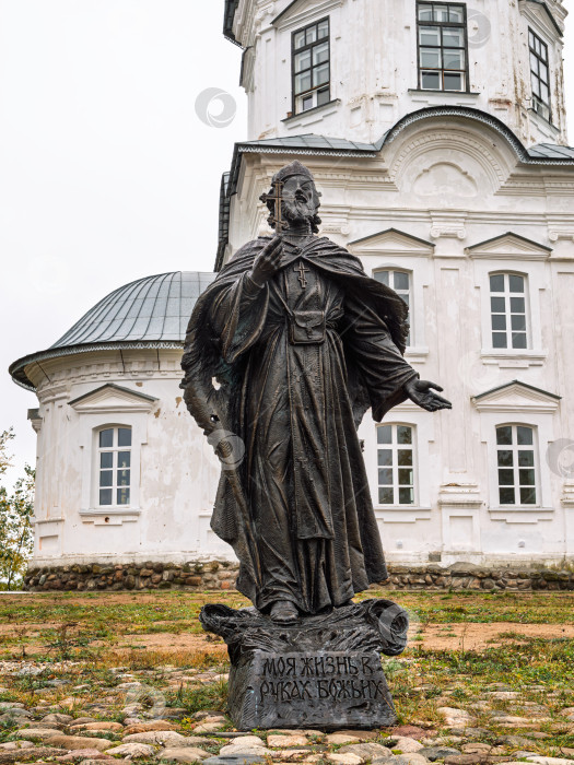 Скачать Памятник герою-монаху иеромонаху Амвросию Матвееву на фоне Крестовоздвиженской церкви в Ниловой пустыни. Бронзовая скульптура с крестом в руках. фотосток Ozero