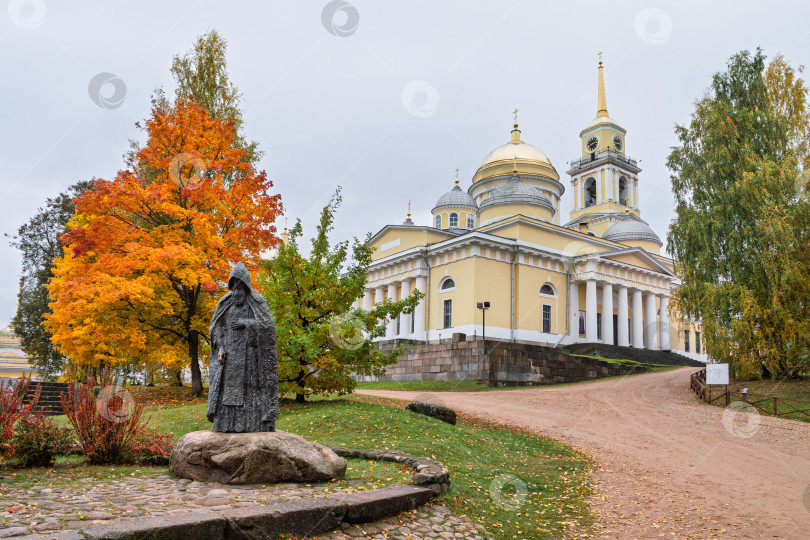 Скачать Живописный осенний пейзаж с памятником преподобному Нилу Столобенскому на огромном камне-валуне в Ниловой пустыни. Бронзовая скульптура на фоне Преображенского собора и колокольни. фотосток Ozero