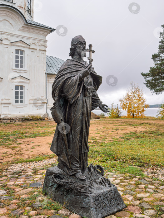 Скачать Памятник герою-монаху иеромонаху Амвросию Матвееву на фоне Крестовоздвиженской церкви в Ниловой пустыни. Бронзовая скульптура в живописном осеннем пейзаже. фотосток Ozero