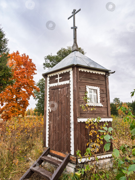 Скачать Крупный план деревянной часовни с крестом на фоне яркого осеннего клена. Святыня на озере Селигер. фотосток Ozero