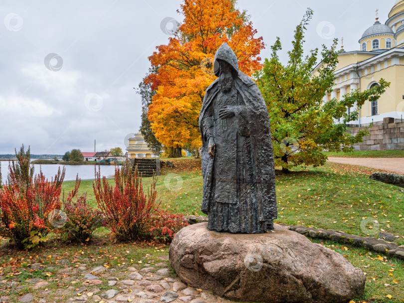 Скачать Живописный осенний пейзаж с памятником преподобному Нилу Столобенскому на огромном камне-валуне в Ниловой пустыни. Бронзовая скульптура на фоне Преображенского собора и Архиерейской пристани. фотосток Ozero