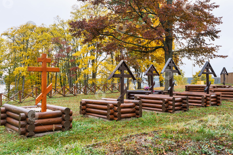 Скачать Уединенное монастырское кладбище Нило-Столбенского монастыря (Нилова пустынь). Деревянные срубы могил с православными крестами на фоне золотой осенней листвы. фотосток Ozero