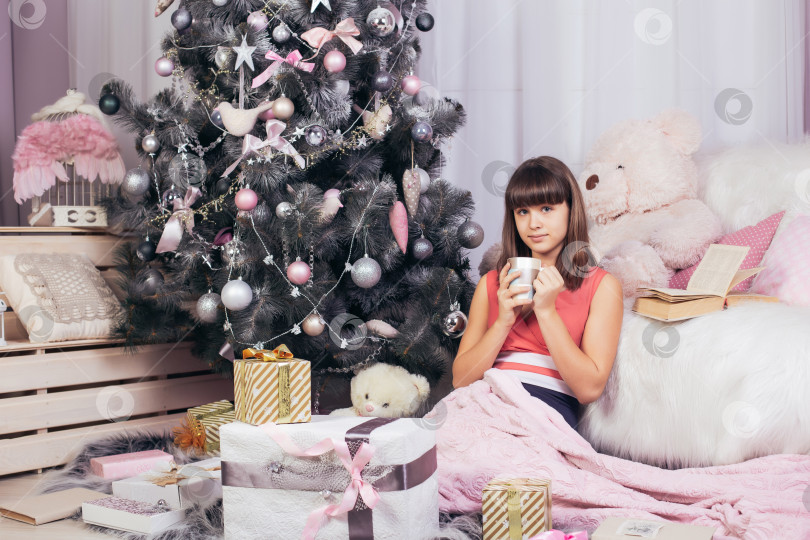 Скачать Девушка пьет напиток, сидя в рождественской гостиной фотосток Ozero