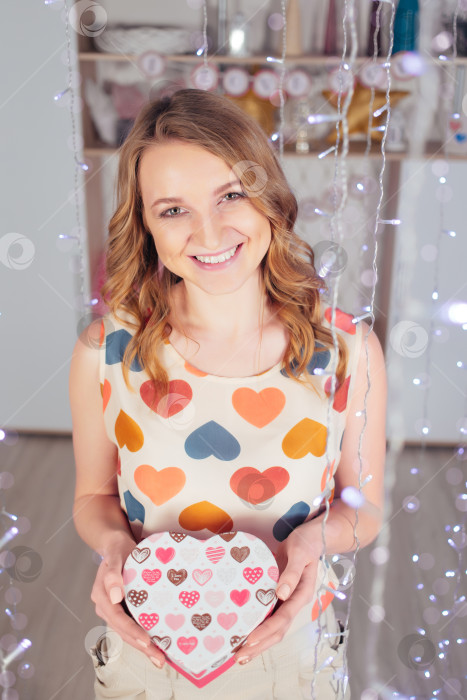 Скачать Молодая красивая женщина с подарком и гирляндами улыбается в День святого Валентина фотосток Ozero