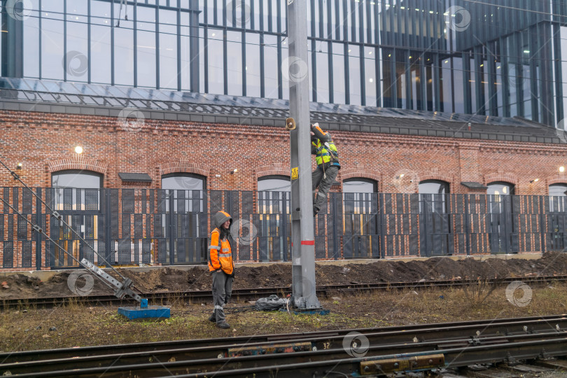 Скачать Рабочие устанавливают систему оповещения на столбе на железной дороге на фоне промышленных зданий. фотосток Ozero