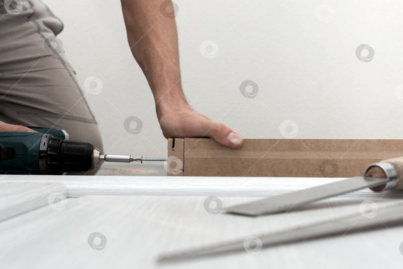 Скачать Рабочий затягивает дверную раму шурупом.  фотосток Ozero