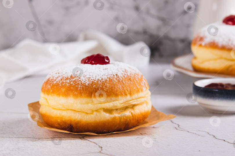 Скачать Вкусные пончики с вареньем в сахарной пудре на пергаментной бумаге на столе фотосток Ozero