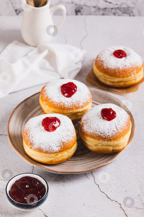 Скачать Вкусные пончики с начинкой из джема и сахарной пудрой на тарелке на столе в вертикальном положении фотосток Ozero