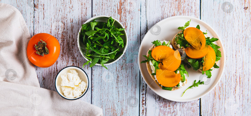 Скачать Хурма, зелень и сливочный сыр в чиабатте на тарелке на столешнице посмотреть веб-баннер фотосток Ozero