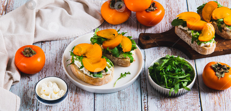 Скачать Сладкие бутерброды с рикоттой, рукколой и хурмой на тарелке на столовом веб-баннере фотосток Ozero