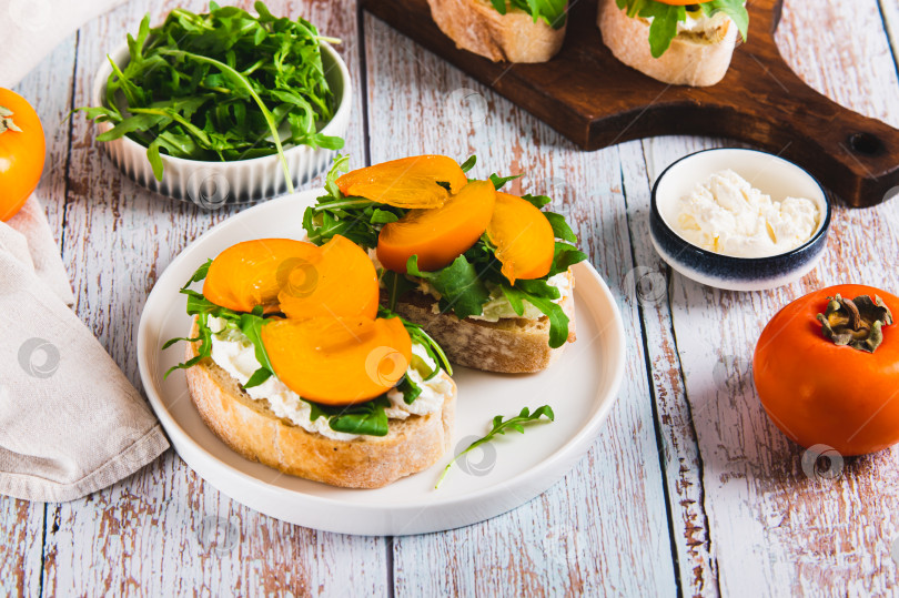 Скачать Хурма, зелень и сливочный сыр на тарелке с чиабаттой на столе фотосток Ozero