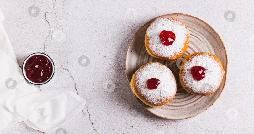 Скачать Вкусные пончики с начинкой из джема и сахарной пудрой на тарелке на столешнице посмотреть веб-баннер фотосток Ozero