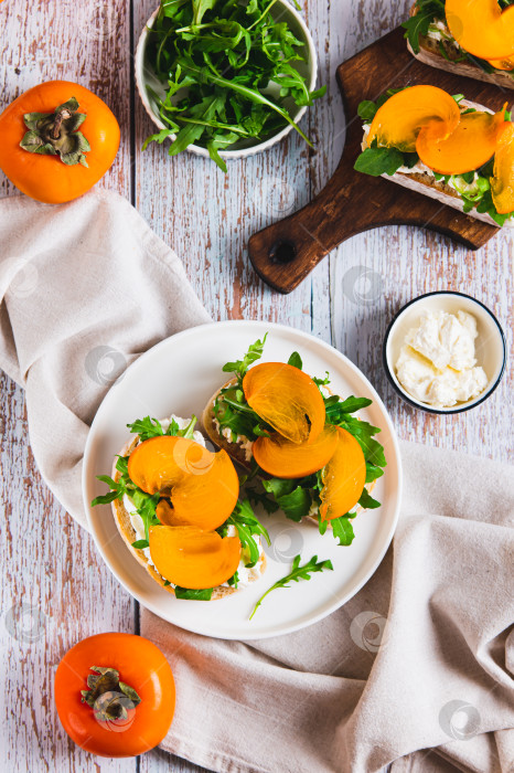 Скачать Хурма, зелень и сливочный сыр в чиабатте на тарелке, установленной на столешнице, в вертикальном положении фотосток Ozero