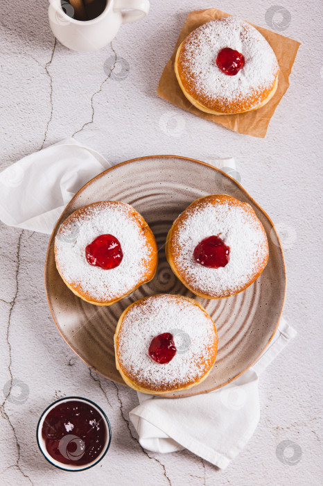 Скачать Вкусные пончики с начинкой из джема и сахарной пудрой на тарелке, установленной на столешнице вертикально фотосток Ozero