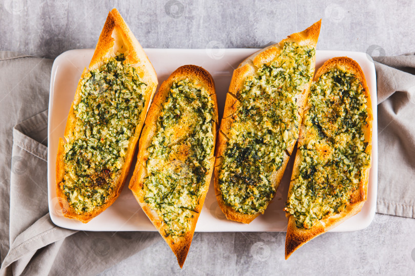 Скачать Запеченный багет крупным планом с маслом, чесноком и укропом на тарелке на столе, вид сверху фотосток Ozero