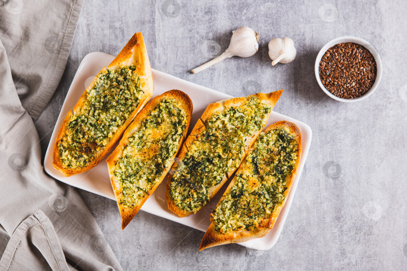 Скачать Запеченный багет со сливочным маслом, чесноком и укропом на тарелке на столе вид сверху фотосток Ozero