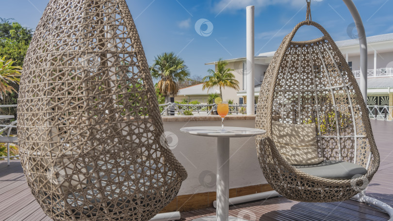 Скачать Плетеные из ротанга подвесные кресла-качели на террасе. фотосток Ozero