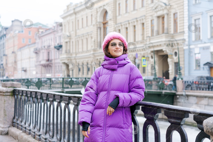 Скачать На мосту стоит женщина в фиолетовом пальто и розовой шляпе фотосток Ozero