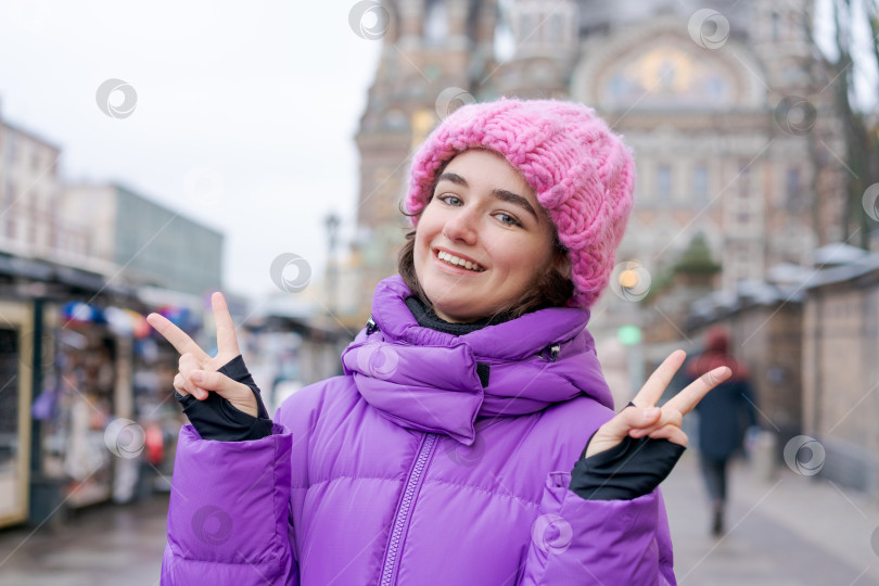 Скачать Женщина в фиолетовом пальто и розовой шляпе улыбается и подает знаки мира фотосток Ozero