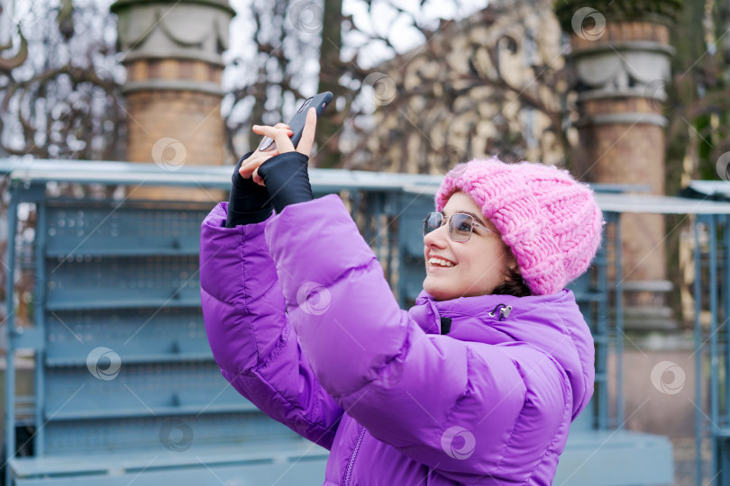 Скачать Женщина в фиолетовом пальто и розовой шляпе делает снимок на свой мобильный телефон фотосток Ozero