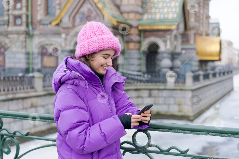 Скачать Женщина в фиолетовом пальто улыбается и смотрит в свой мобильный телефон фотосток Ozero