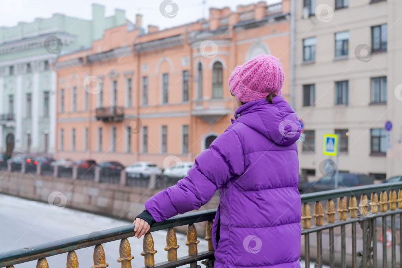 Скачать Женщина в фиолетовом пальто стоит на мосту и смотрит на воду фотосток Ozero