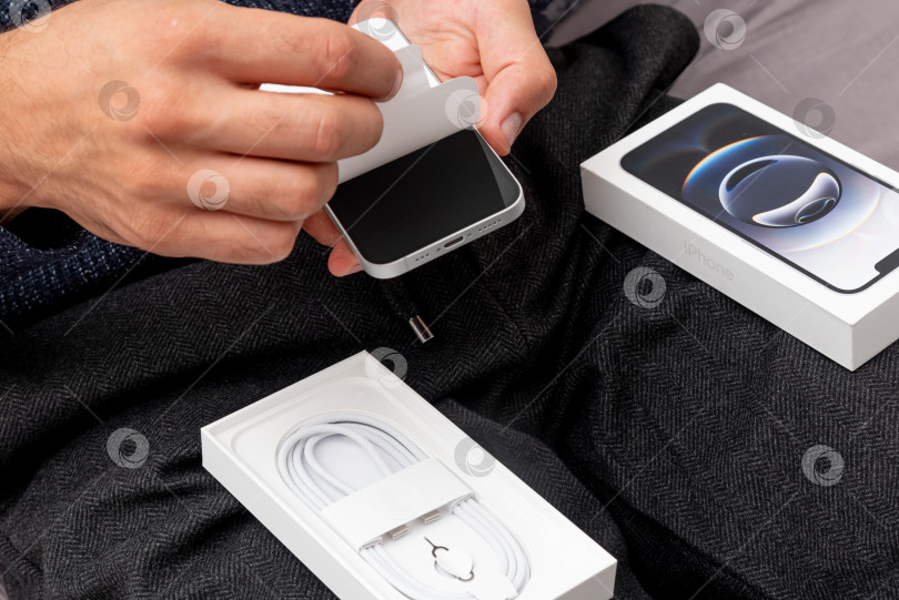 Скачать Бар, Черногория, 2 ноября 2025 года, Мужчина срывает защитную пленку с экрана iPhone фотосток Ozero