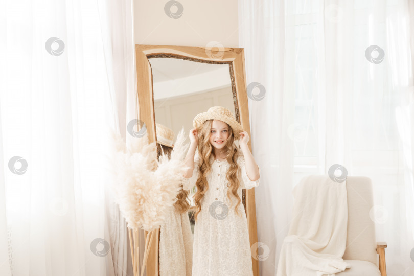 Скачать Красивая девочка-подросток с длинными волосами примеряет соломенную шляпку перед зеркалом. Самолюбование блондинки. фотосток Ozero