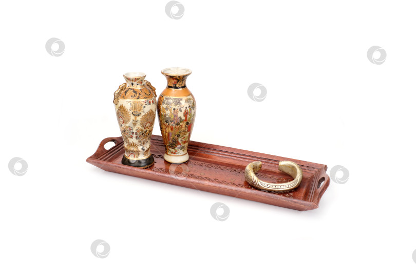 Скачать Деревянный резной декоративный поднос ручной работы на белом фоне. На подносе изображен натюрморт с двумя китайскими вазами и серебряным браслетом фотосток Ozero