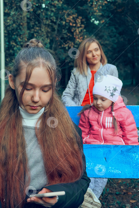 Скачать Фотография с разными точками фокусировки, выборочный фокус. Мама и две дочери сидят на скамейках. Старшая дочь на переднем плане находится в центре внимания, остальные в фокусе. Отдых фотосток Ozero