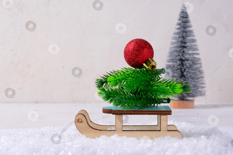 Скачать Красный елочный шар и еловые ветки на игрушечных деревянных санках в искусственном снегу фотосток Ozero