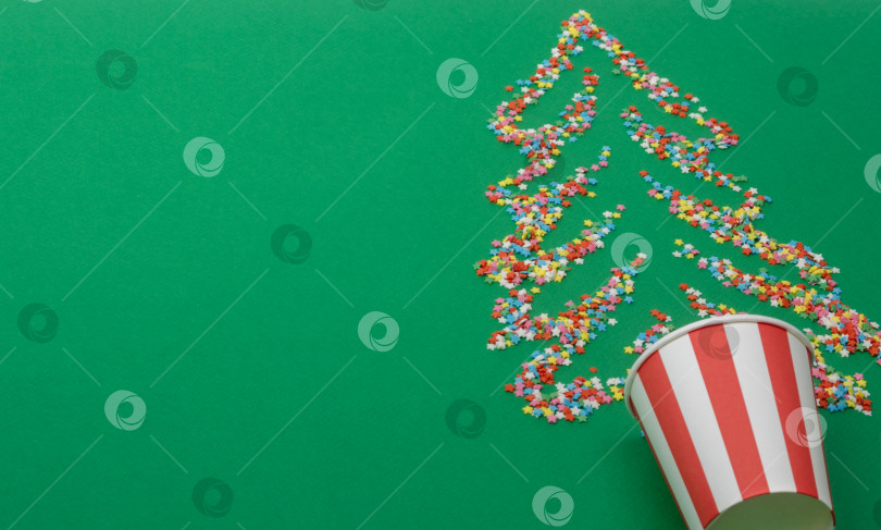 Скачать На зеленом фоне разбросаны разноцветные сахарные звездочки в форме рождественской елки. На зеленом фоне также размещен бумажный стаканчик фотосток Ozero