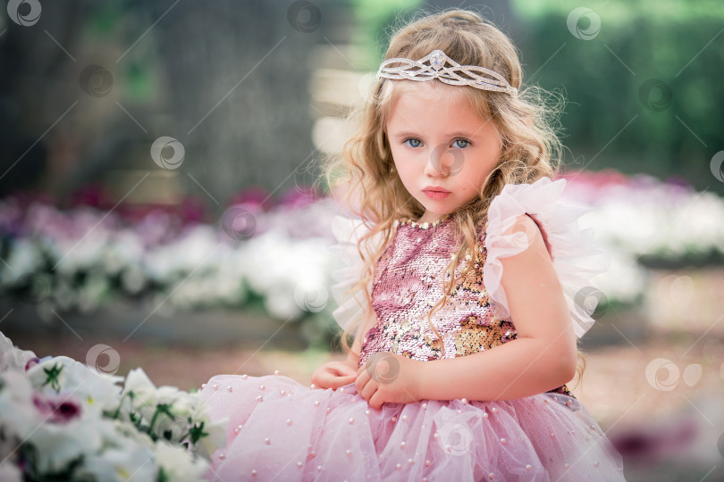 Скачать Девушка в розовом платье, с диадемой и длинными вьющимися волосами смотрит в камеру. Концептуальный портрет детства. фотосток Ozero