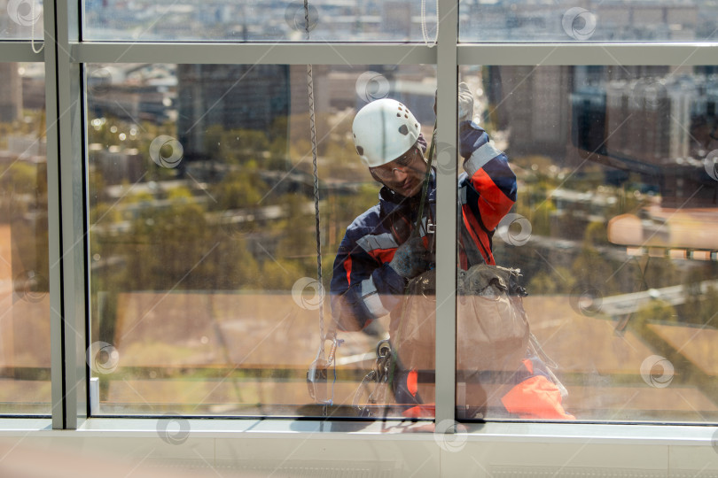 Скачать Мужчина, промышленный альпинист или мойщик окон, на веревке моет окна небоскреба. фотосток Ozero