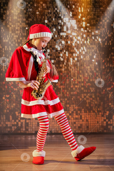 Скачать Маленькая девочка в костюме Санта-Клауса играет на саксофоне. фотосток Ozero